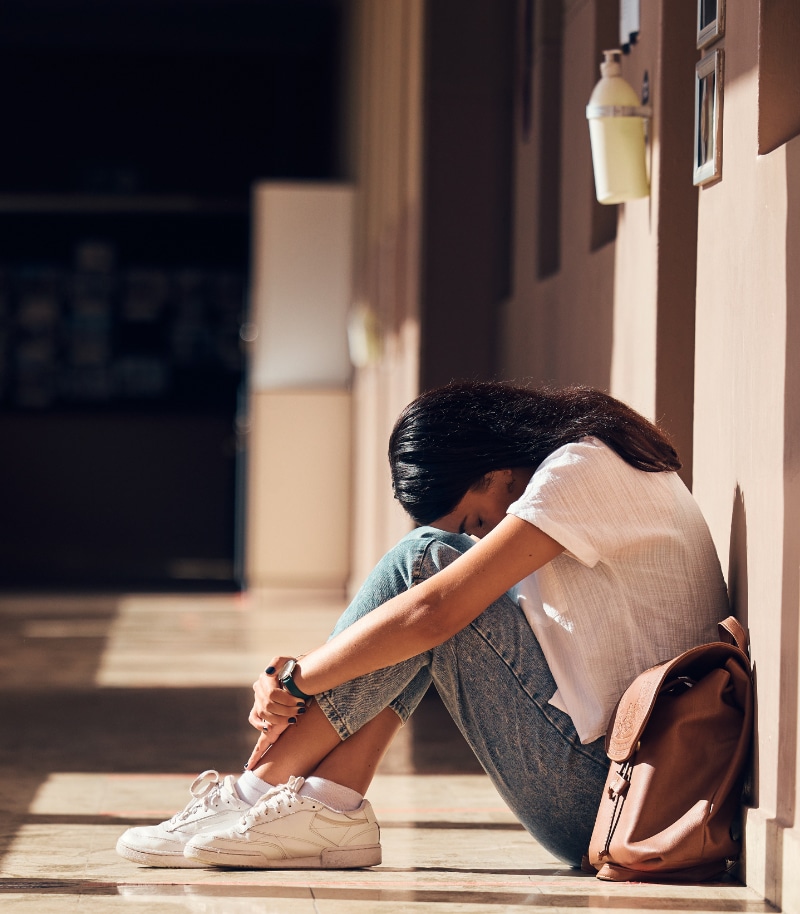 Sad, lonely and girl with depression at school, crying and anxiety after bullying. Mental health, tired and unhappy student in the corridor after problem in class, education fail and social isolation